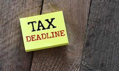 TAX DEADLINE words on a small yellow sheet of paper and a wooden table