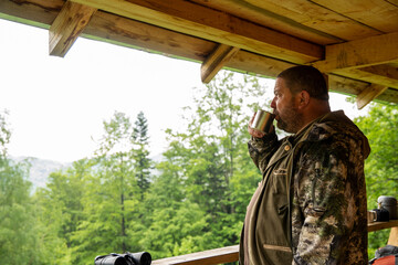 Hunter with his shotgun in middle of nature. Male hunter hunting outdoors, drinks black coffe in...