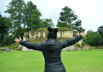 Mujer latina con los brazos abiertos mirando hacia un templo en las Ruinas de Iximche en Guatemala. - obrazy, fototapety, plakaty