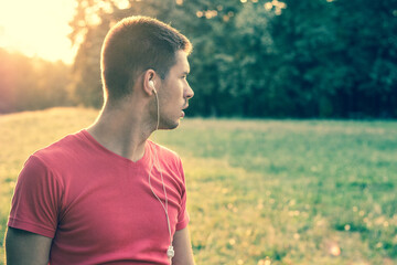 Beautiful man with headphones, outdoors, nature. Man listening to music in the forest nature sunset