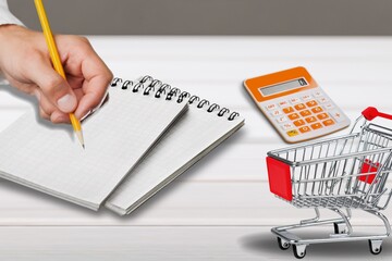 Man calculates the budget. Shopping cart a on table with calculator and paper. Rising food and...