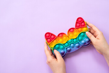 Woman using pop it fidget toy on purple background, top view