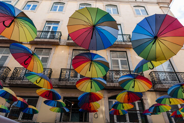 Fototapeta na wymiar Colorful rainbow umbrellas fly in the street near buildings in Lisbon, Portugal. Concept creative idea