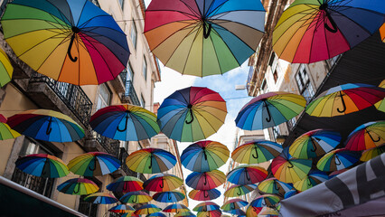 Fototapeta na wymiar Rainbow colored umbrellas hang along the street in Lisbon, Portugal. LGBTQ community concept. Creative Idea