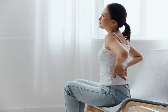 Suffering from scoliosis osteochondrosis after long study pretty young Asian woman feel hurt joint back pain laptop in incorrect posture sit on chair. Injuries Poor health Illness concept. Cool offer