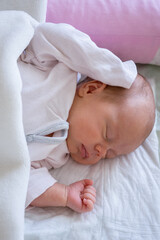 cute little newborn baby girl peacefully sleeps in the nursery on a white cotton bed. vertical