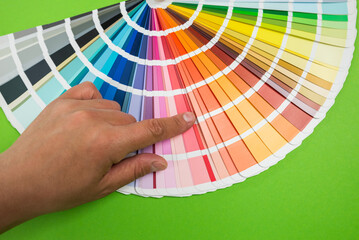 Female hand chooses color in palette swatches. Rainbow colors catalog isolated on green