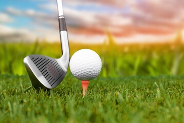 Golf club and ball on green grass ready to be struck on golf course background, evening time.