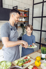 Handsome father and his teenager son spending quality time together. Men doing chores, cooking healthy vegetable salad, tasty food in the kitchen at home