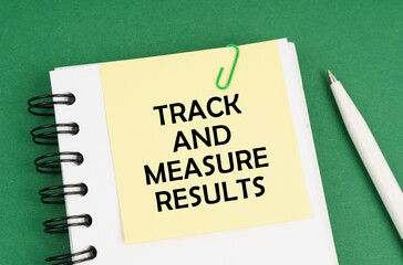 On a green surface, a pen, a notepad with stickers and the inscription - Track And Measure Results