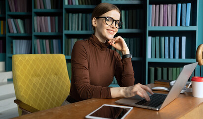 Writes a message in an online chat a woman with glasses works uses a laptop in an office in a coworking space