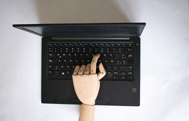 Wooden mannequin hand typing on laptop – AI and technology concept