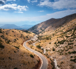 Fototapeta na wymiar Aerial view of winding mountain road, blue sky with clouds at sunrise in summer. Lefkada, Greece. Top view from drone of empty road, orange hills in spring. Beautiful landscape with highway. Travel