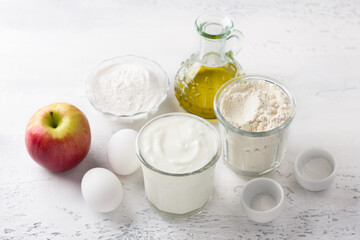Ingredients for apple pancakes: apple, yogurt, wheat and rice flour, eggs, vegetable oil, salt and baking powder on a light gray background, top view. Cooking delicious homemade food.