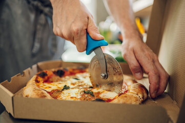 Hand of kitchen chef cutting pizza with a pizza cutter