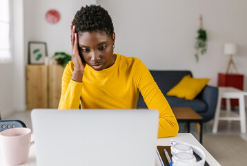 Worried young african woman using laptop at home - Unhappy african american female reading bad news...