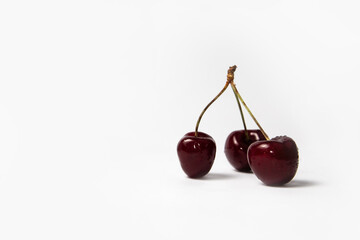 Three red cherries with stems on white background