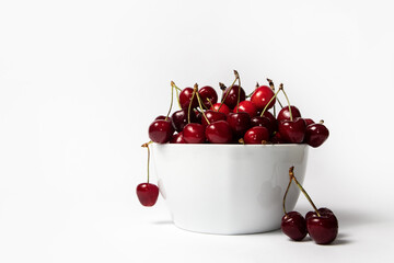 Fresh ripe cherries in a white bowl on white background