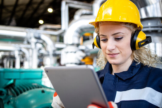 Portrait of petrochemical industrial female worker checking production parameters in oil and gas refinery plant.