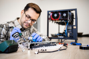 Professional serviceman repairing graphics card and soldering printed circuit board.