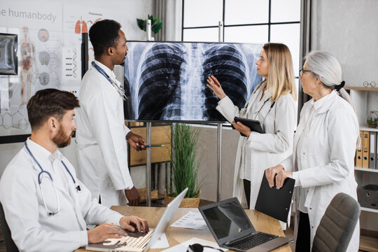 International Team Of Doctors Gathering Together For Discussing Lungs X Ray Result In Progressive Diagnostic Centre. Multiethnic Qualified Staff Having Work Meeting For Searching Ways Of Treatment.