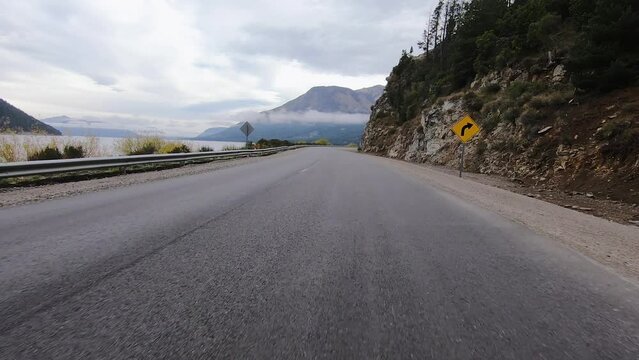 Driving in Patagonia. Traveling along the asphalt road across the forest and besides lake Nahuel Huapi. The Andes mountains in the horizon.