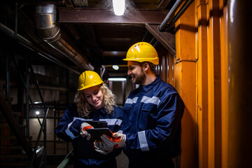 Industrial workers or engineers standing inside factory and checking the computer.