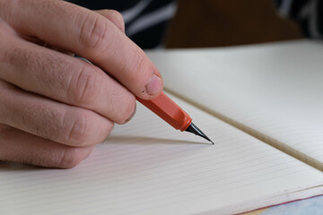 hombre escribiendo en un cuaderno rayado con una pluma y un lapiz