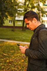 Defocus young man holding phone. Man using smart phone in autumn park. Typing text message or reading social media at mobile phone. Fall background. Cell phone. Communication. Out of focus