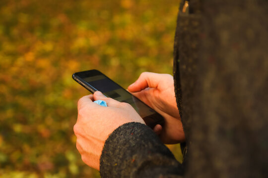 Defocus male hand holding phone. Man using smart phone in autumn park. Typing text message or reading social media at mobile phone. Fall background. Using cell phone. Communication. Out of focus