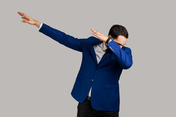 Portrait of positive optimistic businessman standing in dab dance pose, internet meme, celebrating success, wearing official style suit. Indoor studio shot isolated on gray background.