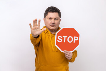 Concentrated serious man looking angrily showing stop gesture, holding road traffic sign, warning...