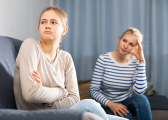 Sad female and daughter sitting at sofa and having quarrel at home