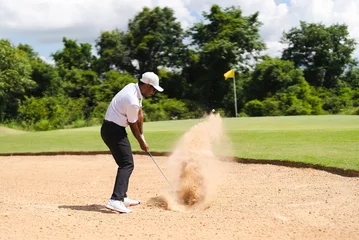 Foto op Plexiglas Asian man golfing on the course. He hits a golf ball on a sand field. © torwaiphoto