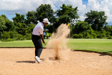 Asian man golfing on the course. He hits a golf ball on a sand field.