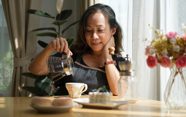 Happy elderly woman drinks coffee in the kitchen at home. Healthy seniors lifestyle.