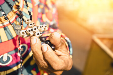 Closeup to the hand of a devotee of santa muerte holding his crucifix of skulls in a cemetery in...