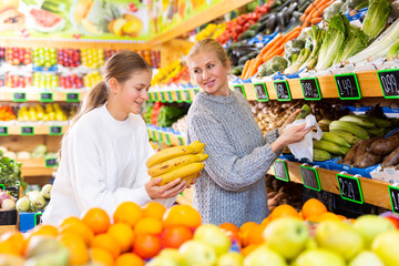 Portrait of teenage girl and her mother who buying fresh vegetables and fruits at grocery shop