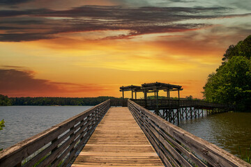 Obraz na płótnie Canvas a brown wooden bridge over the silky green waters of Lake Acworth surrounded by lush green trees and plants with powerful clouds at sunset at Cauble Park in in Acworth Georgia USA