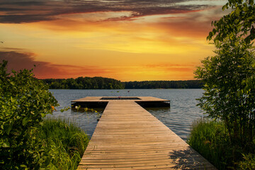 Naklejka na ściany i meble a brown wooden dock over the rippling blue waters of Lake Acworth surrounded by lush green trees and blue with powerful clouds at sunset at Cauble Park in Acworth Georgia USA