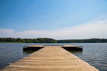a long brown wooden dock over vast blue rippling lake water surrounded by lush green trees with...
