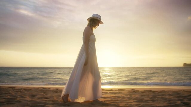 Romantic woman walking by paradise beach and looking around. Lady relaxing on beach against beautiful golden sunset in sea on background. Lady in fashionable trendy boho style dress. Travel vacation