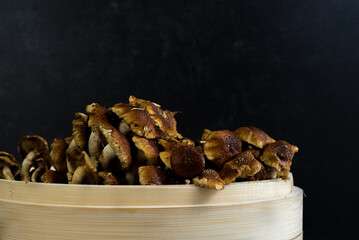 Side of cinnamon cap mushroom in bamboo bowl on dark background