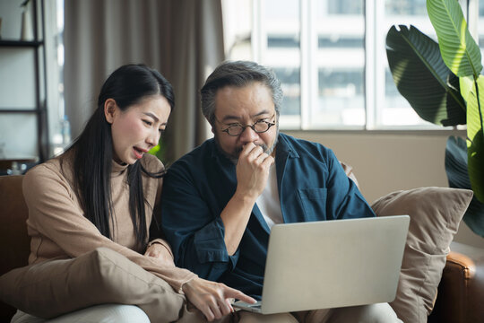 Serious stressed Middle-aged Asian couple finances calculate bills tax on the laptop.