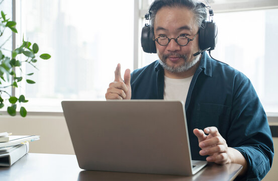 Asian Middle Aged Man Sitting At Home Working On Video Call. Work From Home Concept