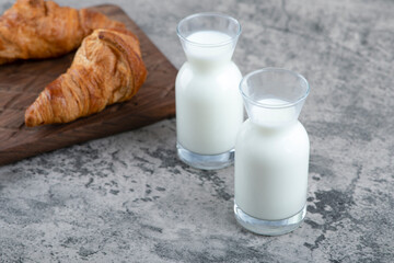A wooden cutting board of fresh croissants and white glass pitchers of milk