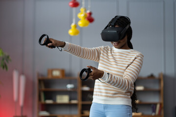 Excite black woman testing virtual reality device in digital world. College student girl hold controllers play shooter vr video game futuristic immersive simulator virtual reality 3D 360 cyber game