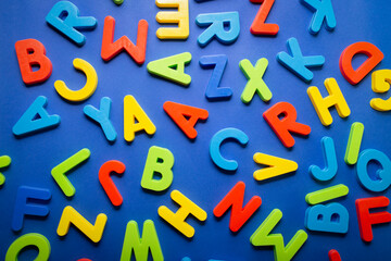 Loose and scattered plastic letters on blue background. Language. Education