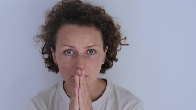 Close-up of the face of a beautiful woman who folded her hands in prayer. A woman who believes in the power of prayer and in God. Sectarian prayers of the Christian faith. Prayer before bed.