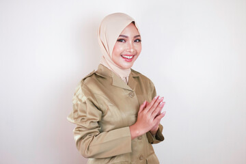 Moslem civil worker wearing brown uniform and hijab greeting with a hand gesture and smiling at the...